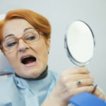 woman looks at teeth in mirror